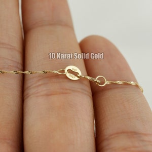 Op de afbeelding: Een close-up van een gouden ketting met een sluiting waarop "10KT ITALY" staat. De ketting heeft een delicaat, gedraaid ontwerp.