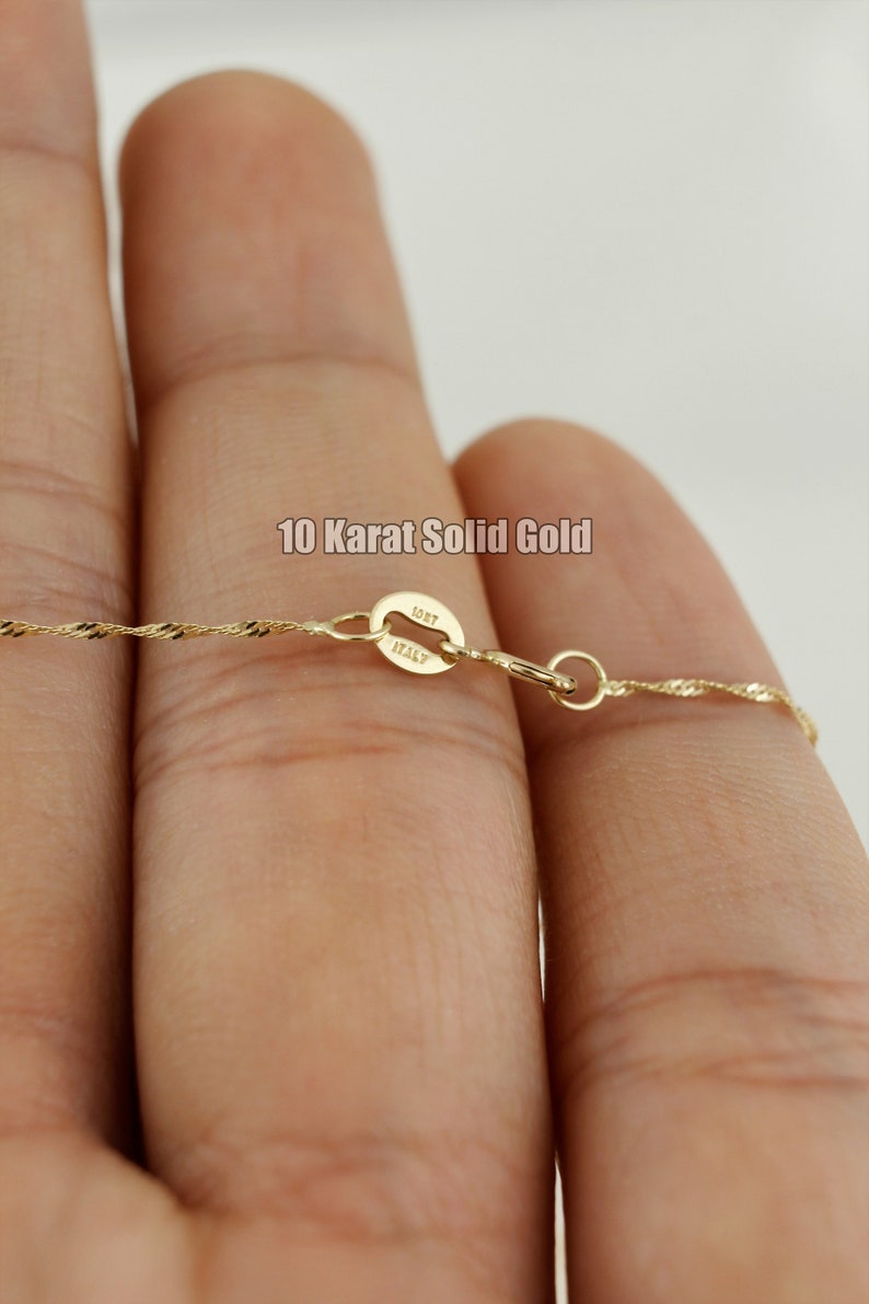 Op de afbeelding: Een close-up van een gouden ketting met een sluiting waarop "10KT ITALY" staat. De ketting heeft een delicaat, gedraaid ontwerp.