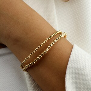 May include: A gold bracelet with a double row of small, textured beads.