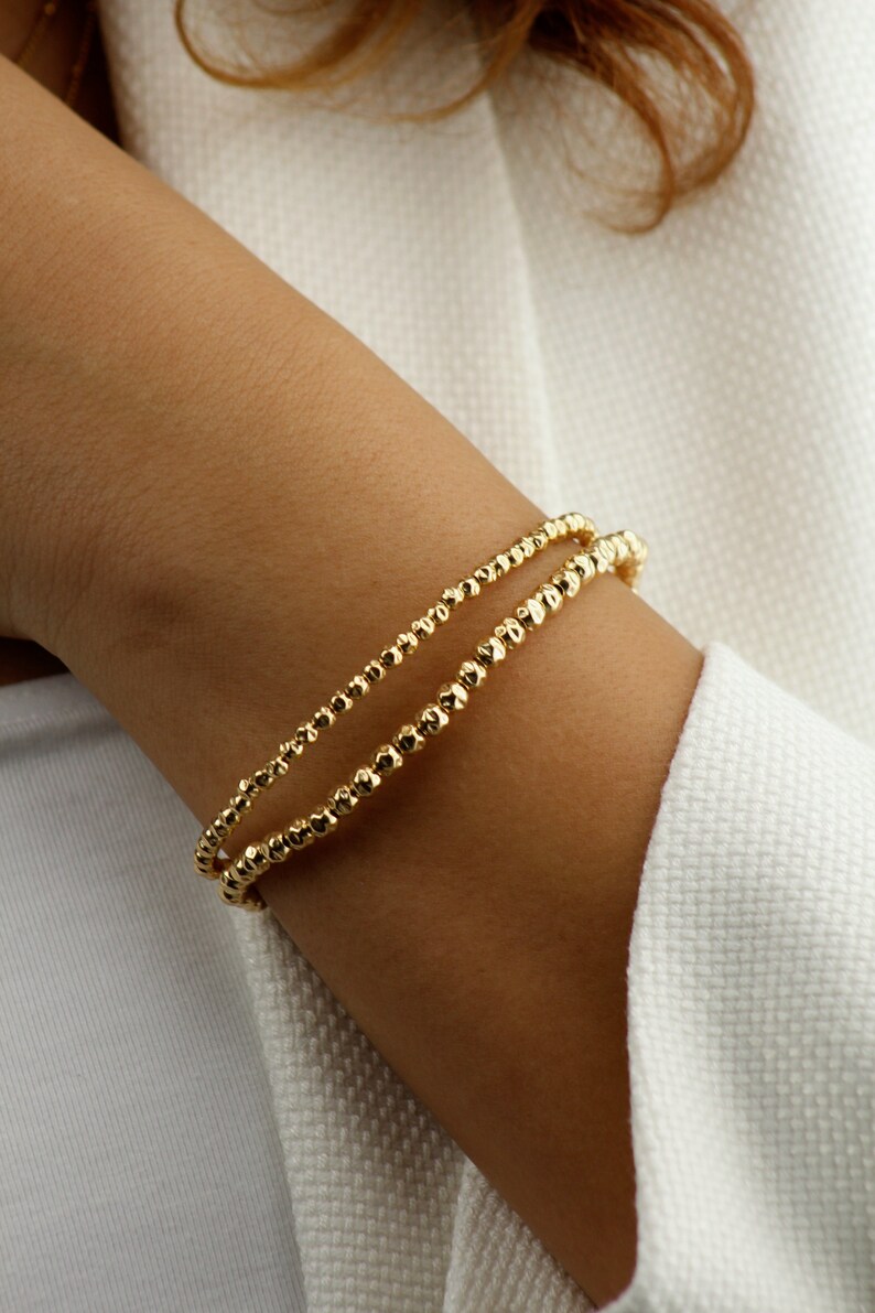 May include: A gold bracelet with a double row of small, textured beads.