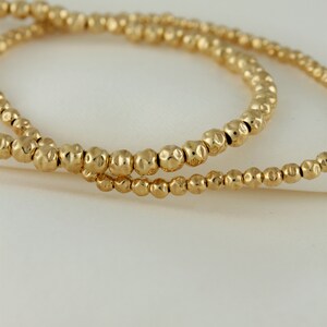 May include: Two gold beaded bracelets with a hammered texture.