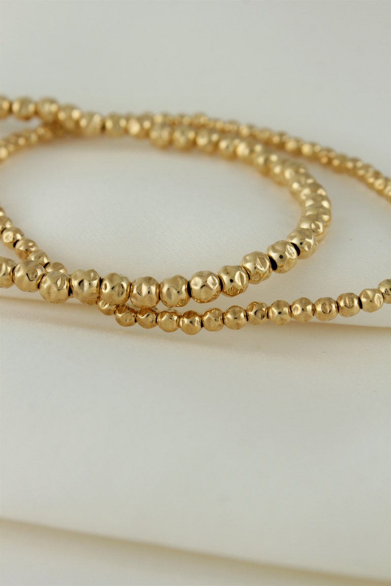 May include: Two gold beaded bracelets with a hammered texture.