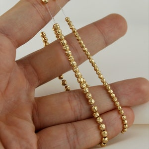 May include: Two gold beaded necklaces with a textured finish. The necklaces are on a hand and are both about 18 inches long.