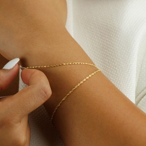 Op de afbeelding: Een gouden kettingarmband met een delicaat touwontwerp. De armband wordt om de pols gedragen.
