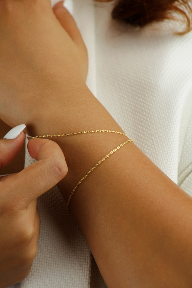 Op de afbeelding: Een gouden kettingarmband met een delicaat touwontwerp. De armband wordt om de pols gedragen.