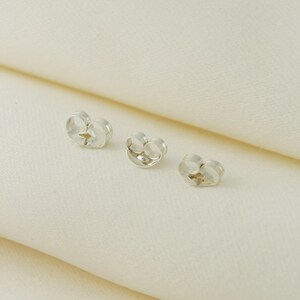 May include: Three silver earring backs, also known as earring stoppers, on a white surface.