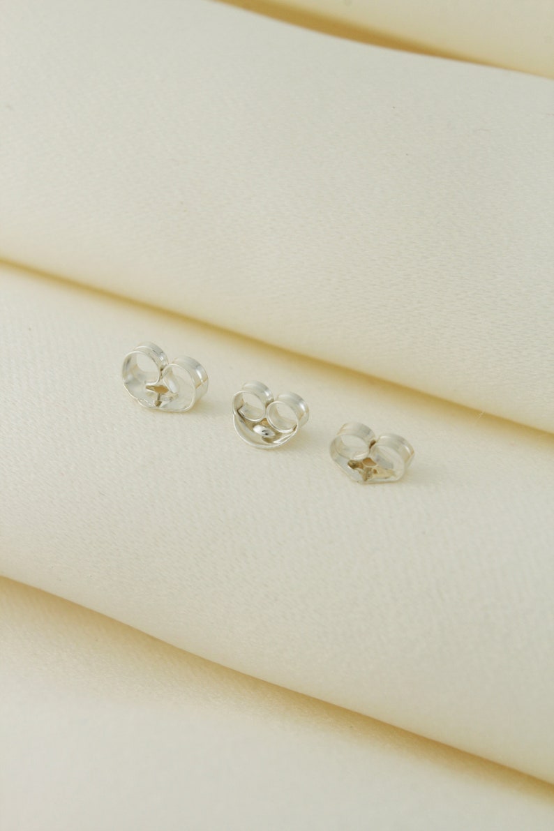 May include: Three silver earring backs, also known as earring stoppers, on a white surface.