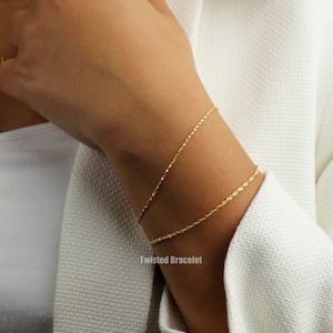 Op de afbeelding: Twee gouden gedraaide kettingarmbanden om de pols van een persoon. De armbanden zijn delicaat en eenvoudig en zouden een geweldig cadeau zijn voor een vriend of geliefde.