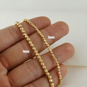 May include: Two gold beaded necklaces, one with 4mm beads and the other with 3mm beads. The necklaces are displayed on a hand.
