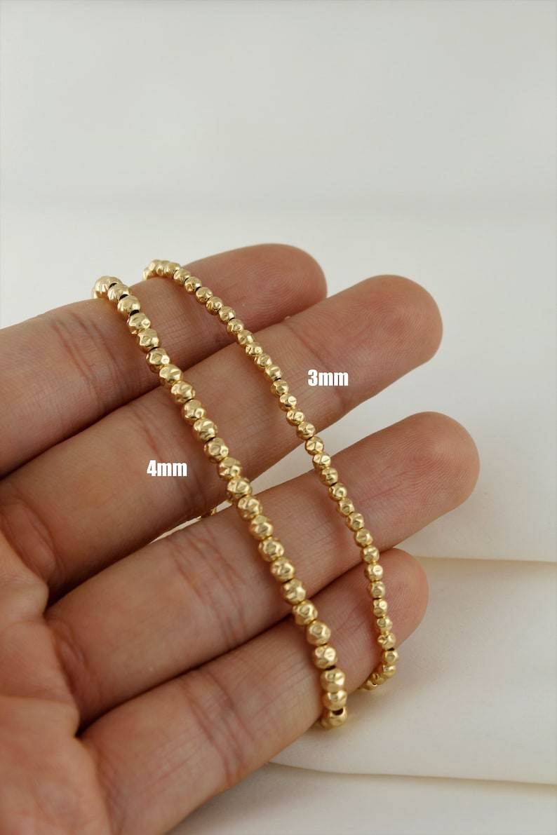 May include: Two gold beaded necklaces, one with 4mm beads and the other with 3mm beads. The necklaces are displayed on a hand.
