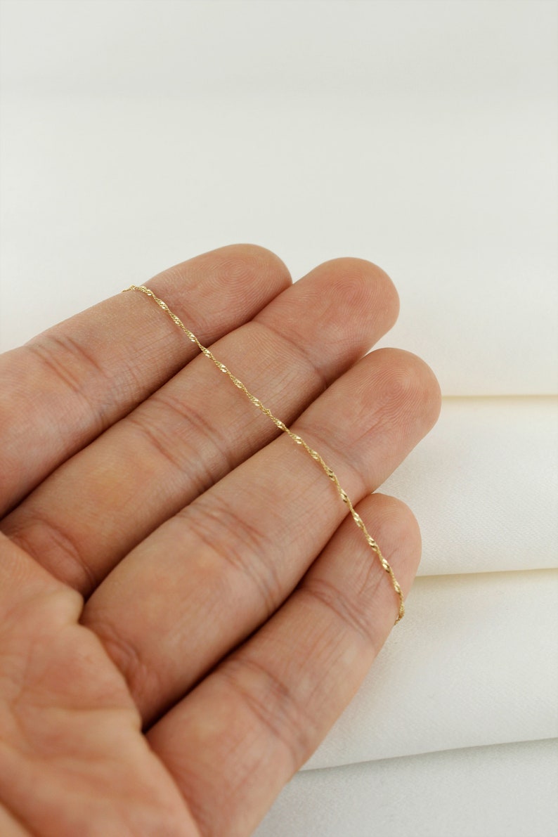 Op de afbeelding: Een dunne gouden ketting met een delicaat, gedraaid ontwerp.