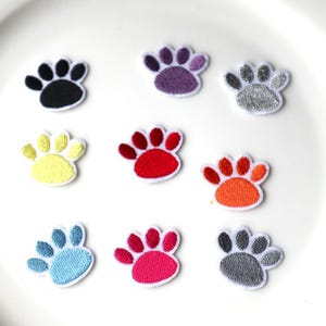May include: Nine embroidered iron-on patches in the shape of a paw print. The patches are in various colours including black, purple, silver, yellow, red, orange, blue, pink, and grey.