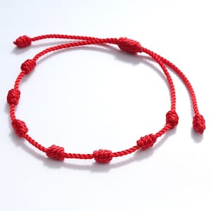 May include: A red string bracelet with multiple knots. The bracelet is made of a thin, braided cord and has a simple design.