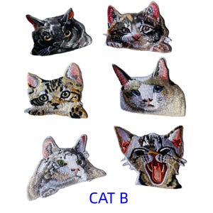 May include: Six embroidered cat head patches featuring various breeds and expressions, including a black cat, a calico, a tabby, a Siamese-style cat, a white and grey cat, and a yawning tabby cat, with the blue text CAT B at the bottom.