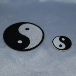 May include: Two embroidered yin yang patches, one larger than the other, on a light blue fabric background. The larger patch is black and white, while the smaller patch is white with a black yin yang symbol.