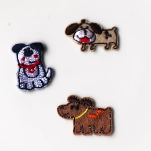 May include: Three embroidered dog patches in different colours. One is light blue with black accents and a red collar. Another is tan with brown ears and a red tongue. The third is brown with yellow and orange details.