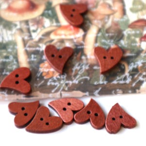 May include: Eight wooden heart-shaped buttons in a reddish-brown colour. The buttons have two holes each.