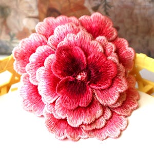 May include: A large, pink and red embroidered flower with a layered design. The flower is made of fabric and has a delicate, feminine look.