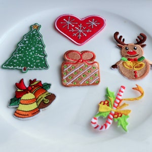 May include: A selection of embroidered Christmas patches on a white plate. The patches include a green Christmas tree, a red heart with snowflakes, a reindeer, a gift, bells, and a candy cane.