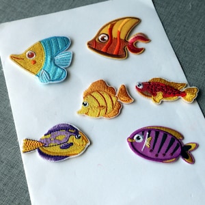 May include: Six embroidered fish patches in various colours. The patches feature detailed stitching and vibrant hues, including yellow, blue, orange, red, and purple. These patches are ideal for adding a decorative touch to clothing or accessories.