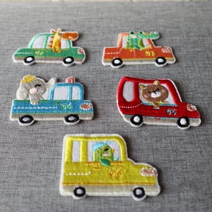 May include: Embroidered patches of cars with animal characters. The patches include a green car with a giraffe, an orange car with a crocodile, a blue car with an elephant, a red car with a bear, and a yellow car with a bird.
