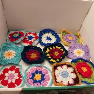 Peut inclure: Une collection de 12 carrés de grand-mère au crochet colorés avec différents motifs de fleurs. Les carrés sont faits avec des fils de différentes couleurs, notamment le rouge, le bleu, le vert, le jaune, le blanc et le violet.
