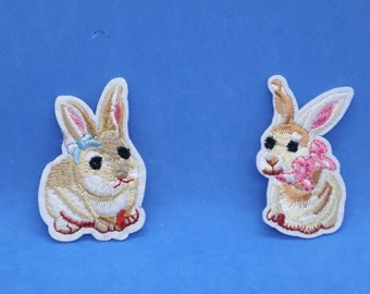 May include: Two embroidered iron-on patches of brown rabbits. One rabbit is wearing a blue bow and the other is holding a pink flower.