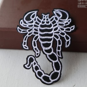 May include: Black embroidered scorpion patch with white stitching. The scorpion is curled up with its tail raised.