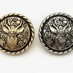 May include: Two decorative buttons with a gold and silver finish. Each button features a detailed design of an antelope head surrounded by floral motifs.
