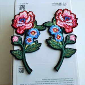 May include: Two embroidered iron-on patches featuring pink, red, white, blue, and green flowers. The patches are on a white background with a printed label that says "Printed with Soy Ink".