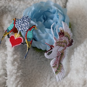 May include: Three embroidered iron-on patches featuring a red heart, a blue and green bird, and a white crane with gold and red accents.