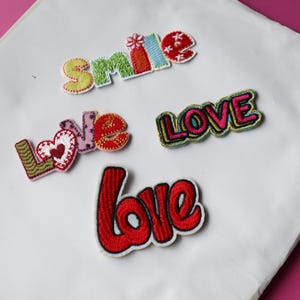 May include: Four embroidered iron-on patches with the words "smile", "love", "LOVE", and "love" in different colours and styles.