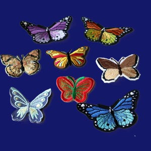 May include: A collection of eight embroidered butterfly patches in various colours and designs. The set includes purple, orange, gold, brown, red, light blue, and dark blue butterflies, each featuring detailed stitching and distinct wing patterns.