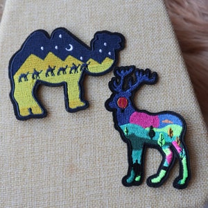 May include: Two embroidered iron-on patches, one of a camel with a starry night sky and the other of a deer with a colorful landscape.