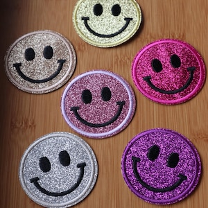 Peut inclure: Six patchs brodables de visage souriant à paillettes de différentes couleurs : or, argent, rose, violet, violet clair et jaune.