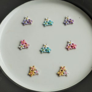 Peut inclure: Huit patchs brodés de fleurs de différentes couleurs, dont le rose, le bleu, le jaune et le violet. Chaque patch présente trois fleurs disposées en forme de triangle.