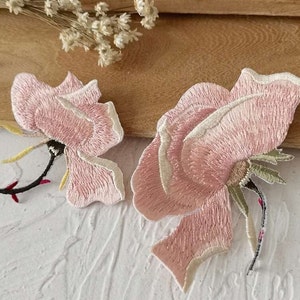 May include: Two pink embroidered rose flower patches. The roses are detailed with white stitching and have green stems.