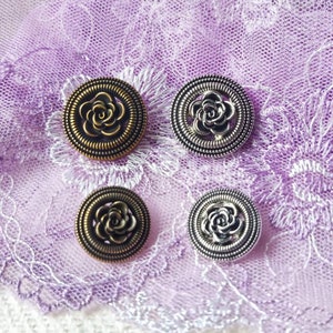 May include: Four decorative buttons featuring a rose design. Two buttons are silver with a black rose and two buttons are gold with a black rose.