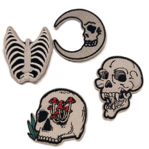 May include: Set of five embroidered iron-on patches featuring various skull designs. The patches include a skull with mushrooms growing out of its head, a skull inside a crescent moon, a ribcage, and two different skull designs.