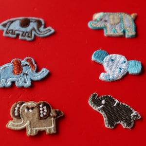 May include: Six embroidered elephant patches in various colors, including blue, brown, and tan, are arranged on a red background. The patches feature detailed stitching and different designs, suitable for crafts or embellishments.