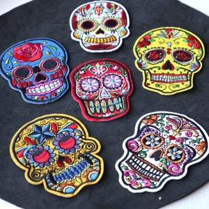 May include: Six colorful embroidered sugar skull patches with intricate designs. The skulls are decorated with flowers, hearts, and stars. The patches are perfect for adding a touch of Mexican culture to your clothing, bags, or other accessories.