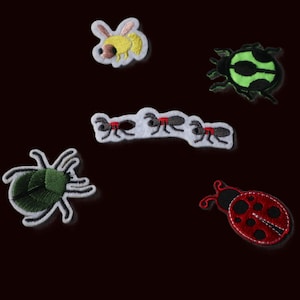 May include: A collection of five embroidered insect patches including a yellow bee, a black and green beetle, a row of three black ants with red accents, a green spider, and a red ladybug with black spots, all featuring white stitched borders.