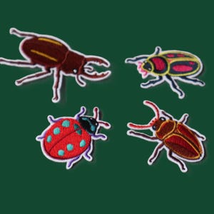 May include: Four embroidered insect patches featuring a brown stag beetle, a colourful beetle with pink and yellow markings, a red ladybug with light blue spots, and a brown beetle with long antennae, all with white borders on a dark green background.