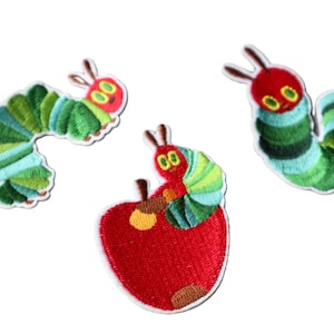 Peut inclure: Écussons brodés représentant une chenille verte et bleue avec une tête et des antennes rouges. Un écusson montre la chenille sur une pomme rouge. Les écussons sont sur fond blanc.