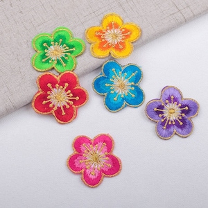 May include: Six colourful embroidered flower patches with gold centres. The patches are in shades of green, orange, blue, red, pink, and purple.