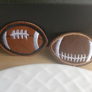 May include: Two brown and white embroidered felt football patches. The patches are approximately 5 cm in diameter.