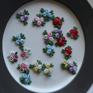 May include: A white plate with a black rim features a variety of embroidered flower appliques in various colors, including pink, blue, red, yellow, and green.
