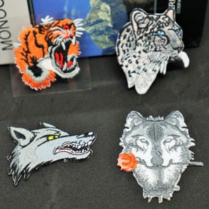 May include: A collection of embroidered animal patches. Designs include a tiger, a leopard, and two wolves, one with a rose. The patches are intricately detailed with various colours and textures, suitable for clothing or accessories.