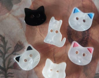 May include: Six cat-shaped buttons, five are white with black eyes and a black nose, one is black with white eyes and a white nose.