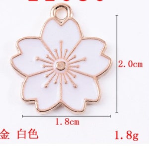 May include: Gold-tone metal charm with a white enamel cherry blossom design. The charm measures 1.8 inches in diameter and weighs 1.8 grams.